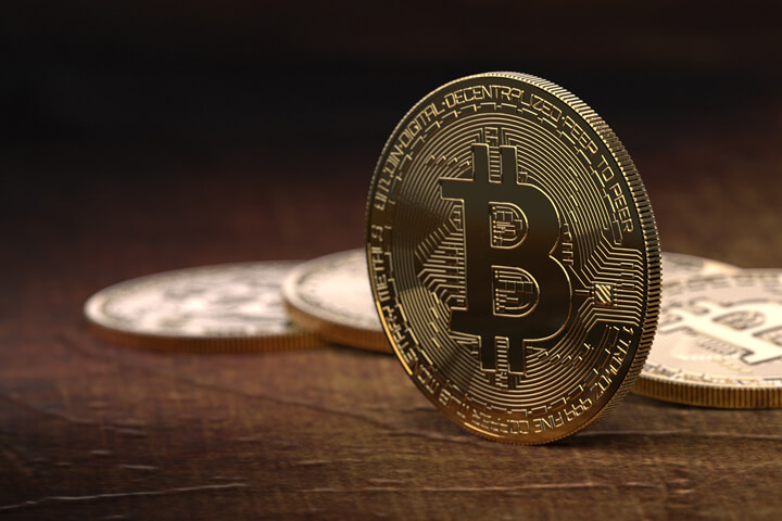 Bitcoin balanced on edge in front of blurred row of other Bitcoins in background