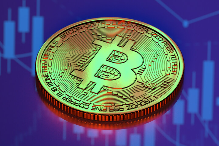 Bitcoin on reflective surface reflecting candlestick chart from monitor