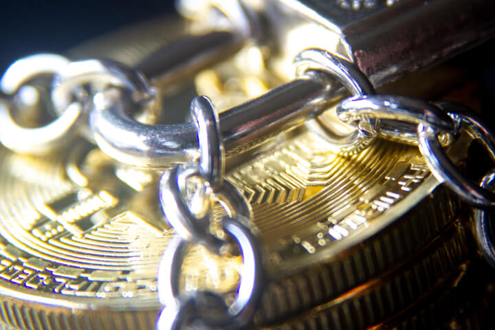 Stack of Bitcoins wrapped with chains and locked with a small padlock