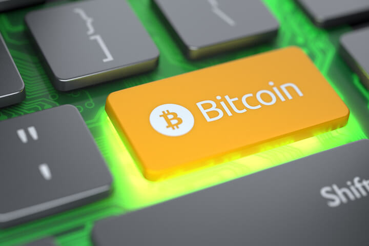 Laptop keyboard with orange Bitcoin key and circuit board glowing with bright light from below