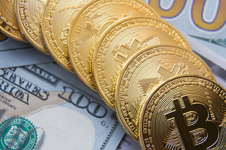 Bitcoins in a curved row on top of US 100 dollar bills