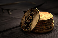 Stack of Bitcoins on rough weathered wood with reading glasses in background