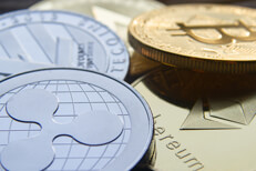 Close up photo of a pile of cryptocurrency coins including Bitcoin, Ripple, Litecoin, Ethereum, and Monero