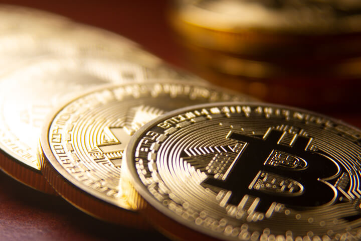 Bitcoins arranged in a row with single coin in background with short depth of field