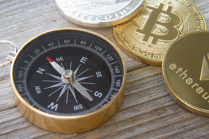 Ethereum coin, Bitcoin, and Litecoin next to navigation compass on wood surface