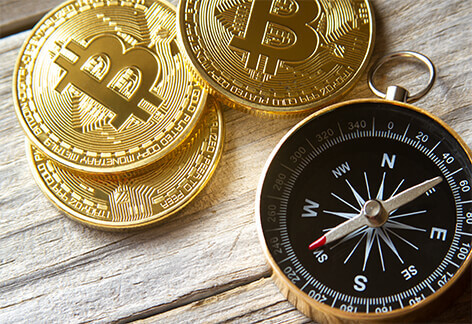 Three bitcoins arranged with navigational compass on weathered wood plank