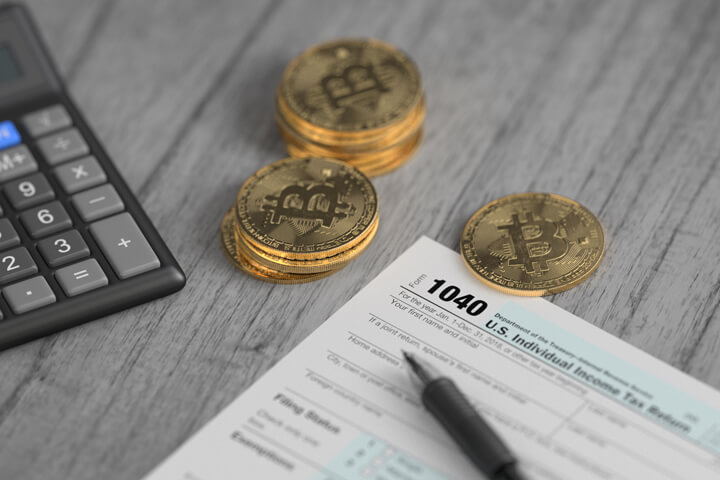 Stacks of Bitcoins surrounding IRS 1040 tax form with ballpoint pen and calculator concept for paying cryptocurrency taxes