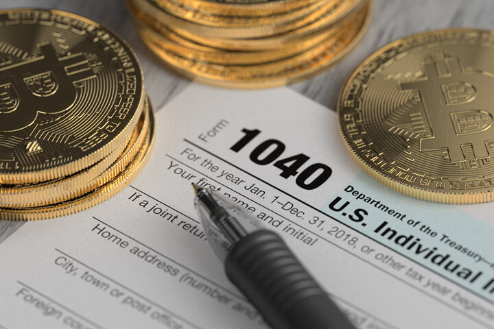 Stacks of Bitcoins surrounding IRS 1040 tax form with ballpoint pen concept for paying cryptocurrency taxes