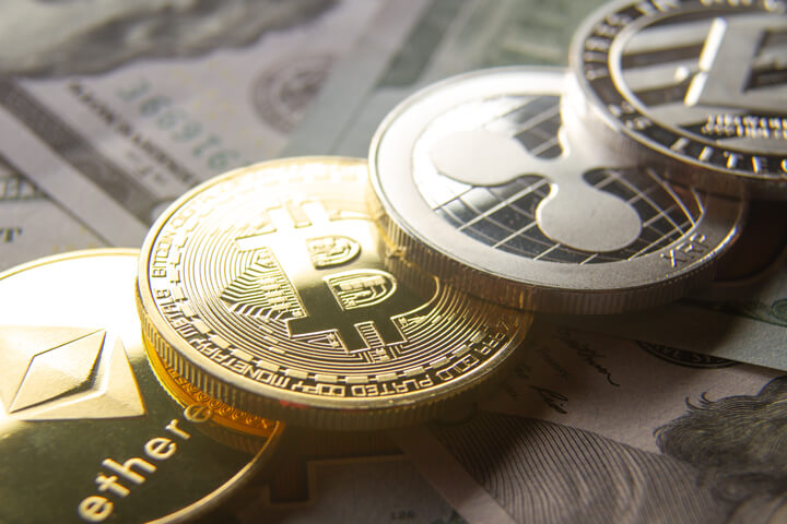 Bitcoin, Ethereum, Litecoin, and Ripple coins in a row on 100 dollar bill background