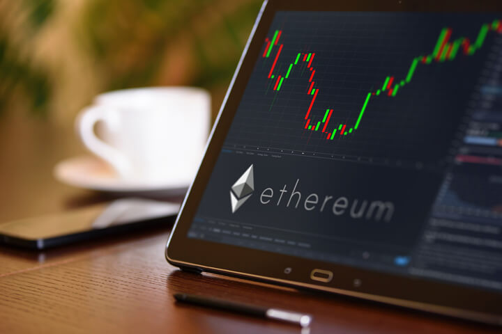 Tablet on desk with coffee cup and cell phone showing Ethereum cryptocurrency logo and stock price candlestick chart