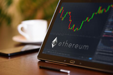 Tablet on desk with coffee cup and cell phone showing Ethereum cryptocurrency logo and stock price candlestick chart