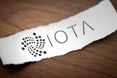 Iota cryptocurrency logo printed on torn piece of white scrap paper lying on woodgrain surface