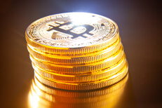 Leaning stack of bitcoins on reflective textured surface with light flare