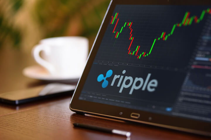 Tablet on desk with coffee cup and cell phone showing Ripple cryptocurrency logo and stock price candlestick chart