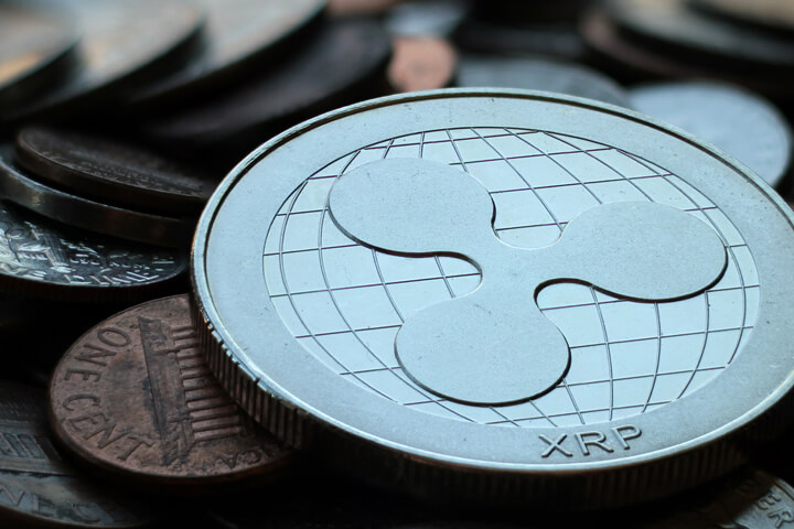 Close up photo of Ripple XRP cryptocurrency coin on top of an assorted pile of tarnished U.S. currency coins