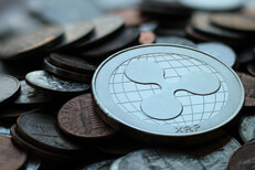 Photo of Ripple XRP cryptocurrency coin on top of an assorted pile of tarnished U.S. currency coins with depth-of-field blur