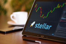 Tablet on desk with coffee cup and cell phone showing Stellar cryptocurrency logo and stock price candlestick chart