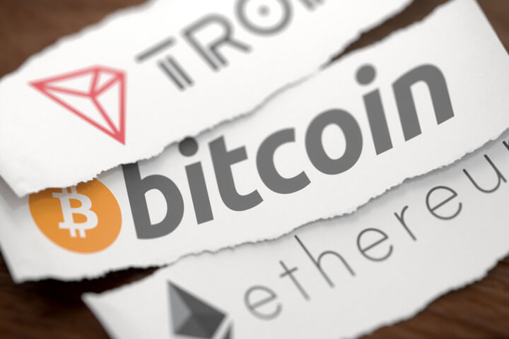 Tron, Bitcoin, and Ethereum cryptocurrency logos printed on torn pieces of white scrap paper on woodgrain surface