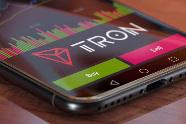 Tron exchange app on iPhone X screen showing Tron logo, trading volume, and option to buy or sell cryptocurrency