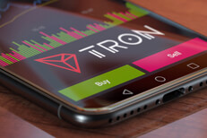 Tron exchange app on iPhone X screen showing Tron logo, trading volume, and option to buy or sell cryptocurrency