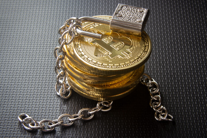 Stack of Bitcoins with unlocked padlock and loose chains on dark carbon fiber background