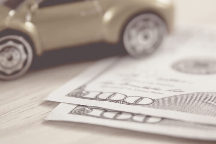 Greyscale version of toy car on wood desk with two one hundred dollar bills