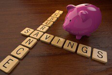 Insurance savings spelled out in wooden letters next to pink piggy bank on desk