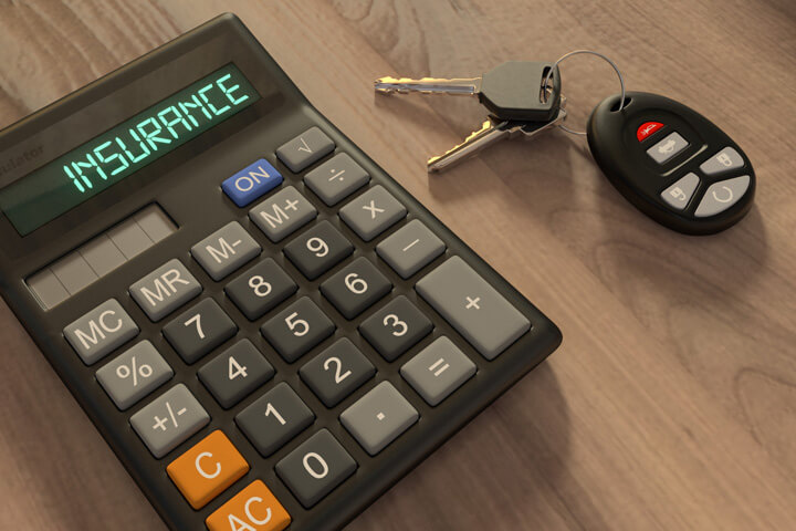 Insurance calculator and car keys on wood desk in morning light