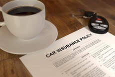 Cup of coffee, car insurance policy, and car keys on wood table