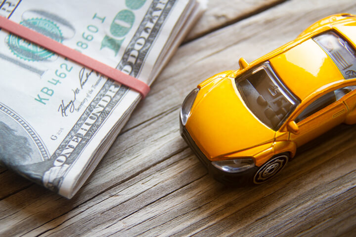 Yellow toy car next to folded 100 dollar bills car insurance or automotive costs concept photo