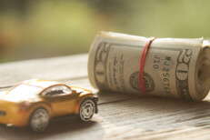 Small toy car next to roll of money wrapped in rubber bands
