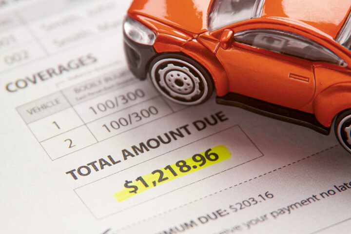 Toy car sitting on car insurance bill with payment due highlighted in yellow