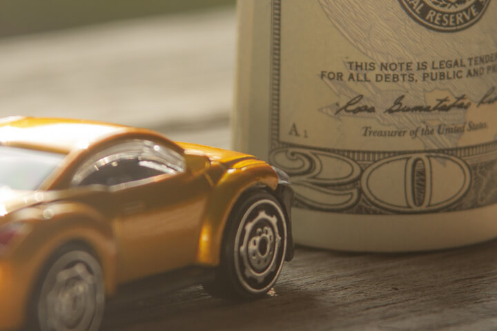 Small yellow car next to upright money roll on wood background
