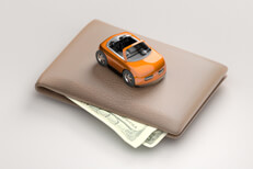 Toy car sitting on top of wallet with corners of bills sticking out from wallet white background