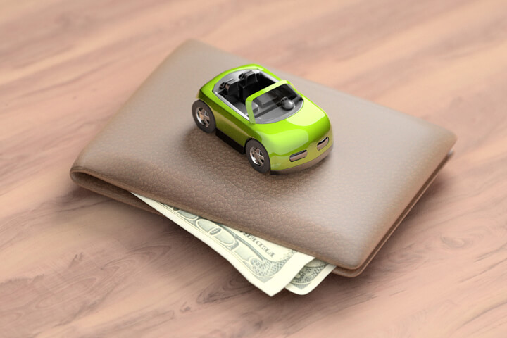 Green toy car sitting on top of wallet with corners of bills sticking out from wallet on wood table