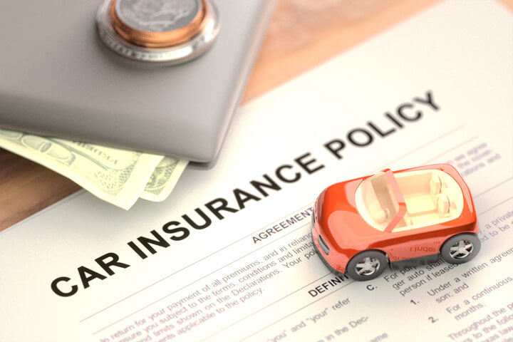 Toy car and wallet with money sitting on paper car insurance policy