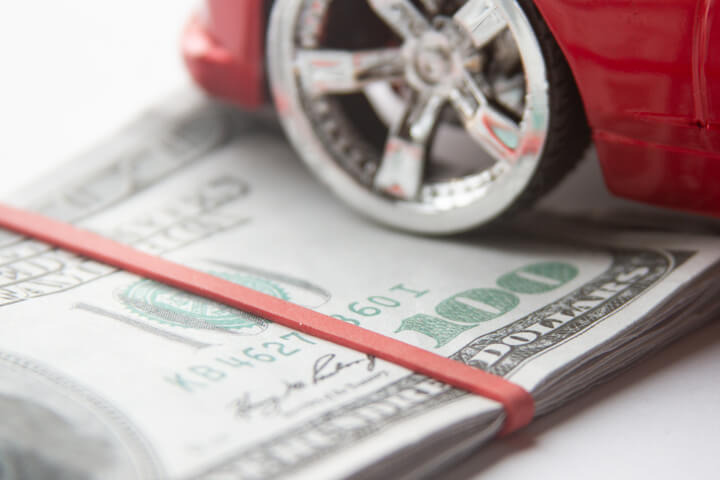 Close view of chrome car wheel and tire resting on folded 100 dollar bills with rubber band