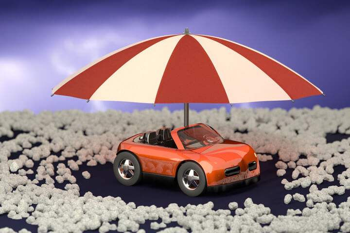 Red toy car with umbrella surrounded by hail stones with stormy sky background