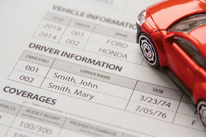 Car insurance policy showing vehicle and driver information with small red toy car