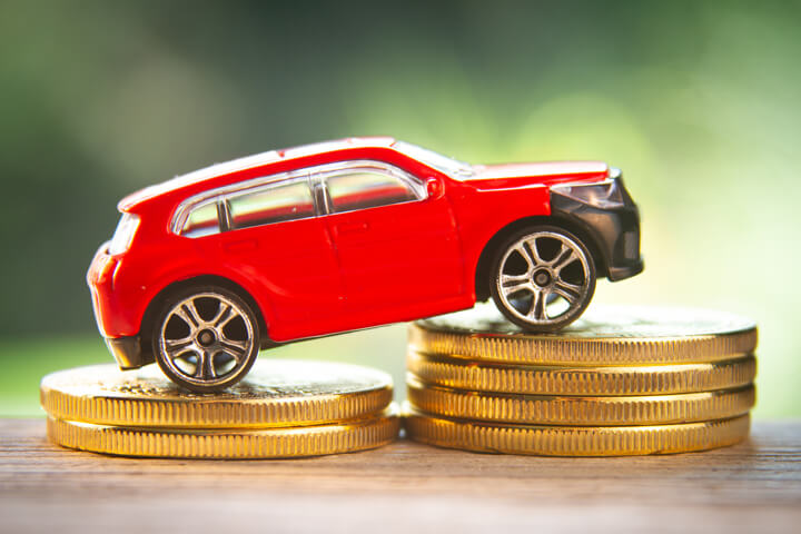 Red toy car on two increasing stacks of gold coins with blurred nature background