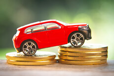 Red toy car on two increasing stacks of gold coins with blurred nature background