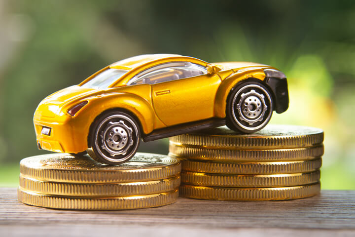 Angled view photo of yellow toy car climbing two stacks of gold coins