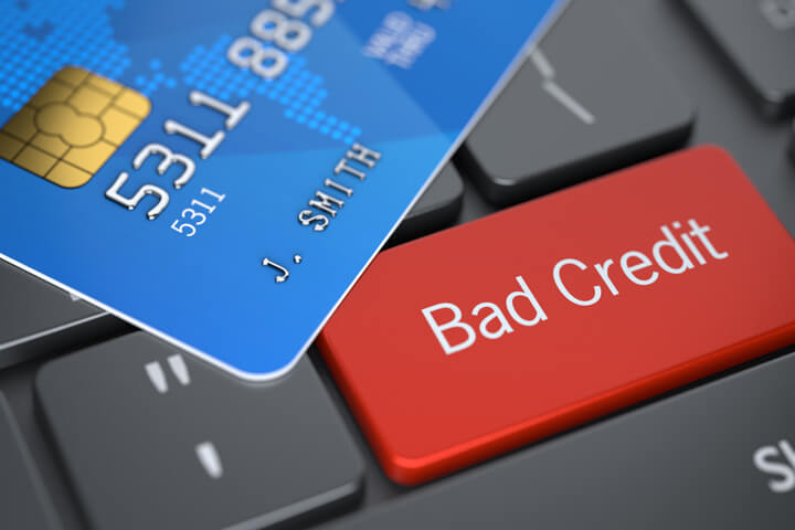 Bright red Bad Credit key on dark laptop keyboard with blue credit card lying on top