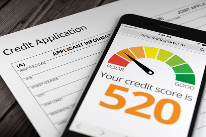 Paper credit application on wood desk with cell phone showing poor credit rating of 520