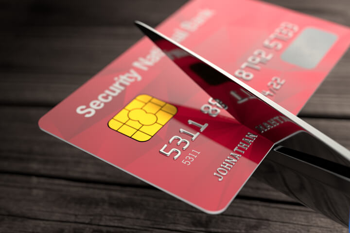 Scissors cutting through red credit card with wood plank background