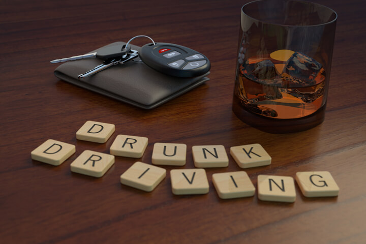 Drunk driving concept showing a glass of whiskey and car keys behind wooden letters spelling drunk driving