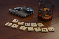Drunk driving concept showing a glass of whiskey and car keys behind wooden letters spelling drunk driving