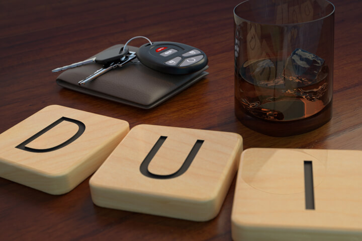 Wood letters spell DUI in front of alcoholic drink and wallet with car keys