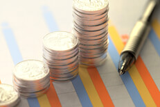 Investment column chart on paper with stacks of coins and pen laying on top