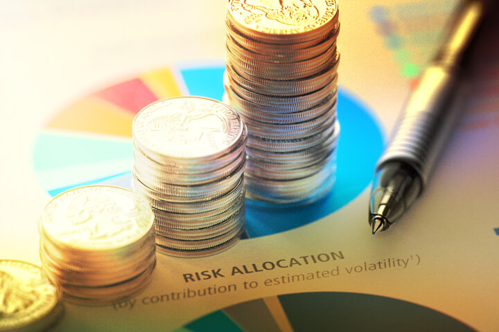 Paper with risk allocation pie chart with increasing stacks of coins and pen
